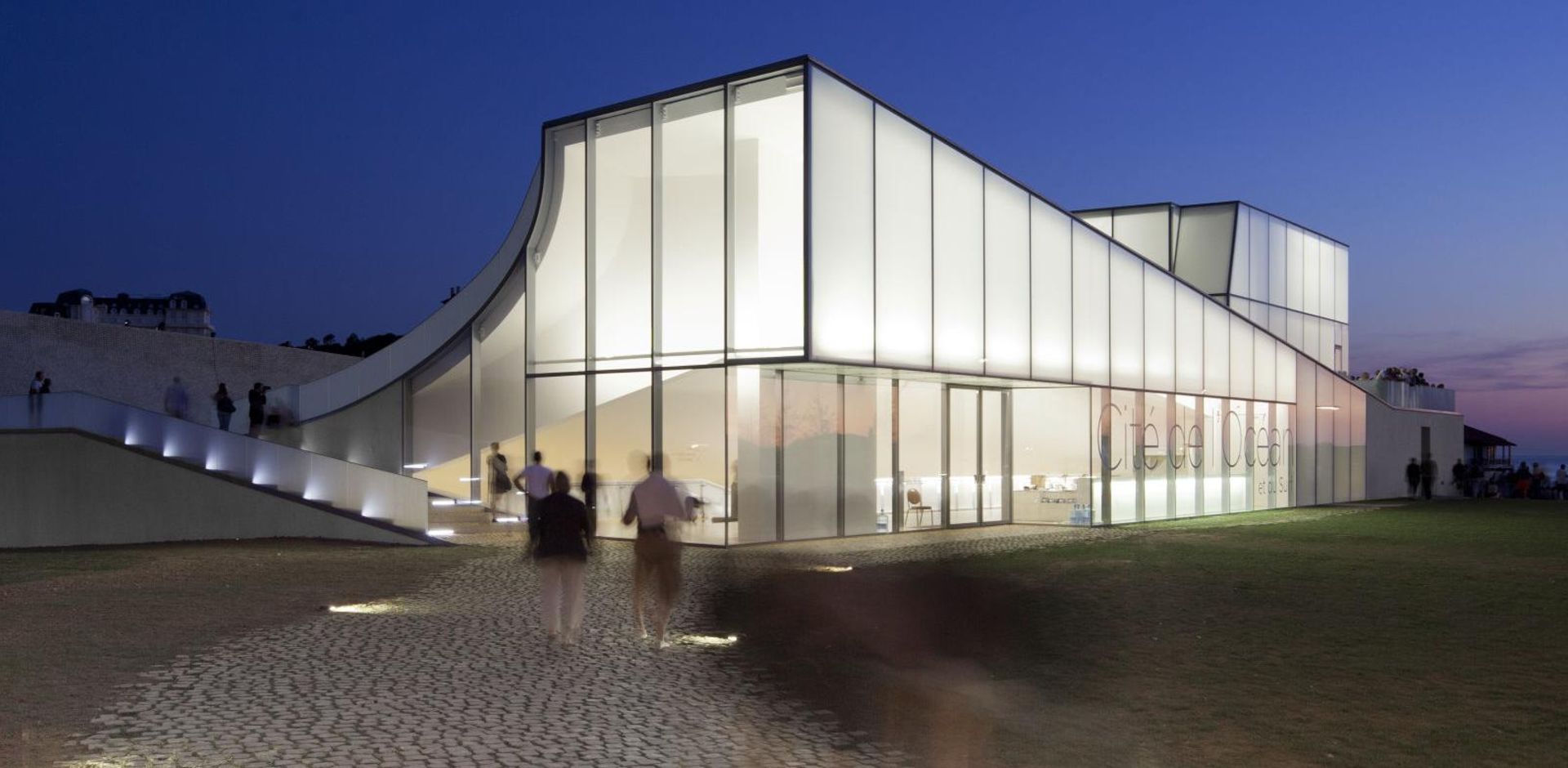 Cité de l'Océan, Biarritz — KAPILUX T glowing white volume at dusk facing the Atlantic