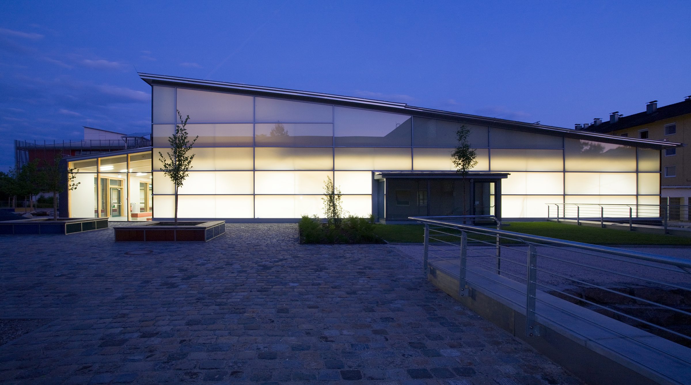 Sporthalle Traunreut exterior at dusk — OKALUX full-wall glazing reading as luminous lantern