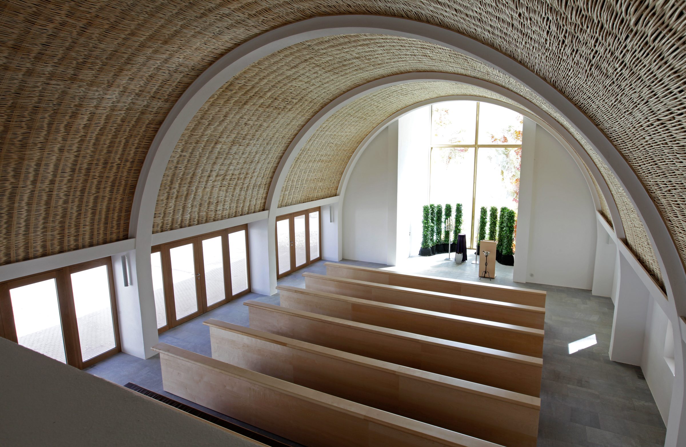 Aussegnungshalle Waldfriedhof nave interior, Aalen, Germany, OKATECH Mandarin woven brass mesh in side-aisle glazing, filtered daylight across chapel interior