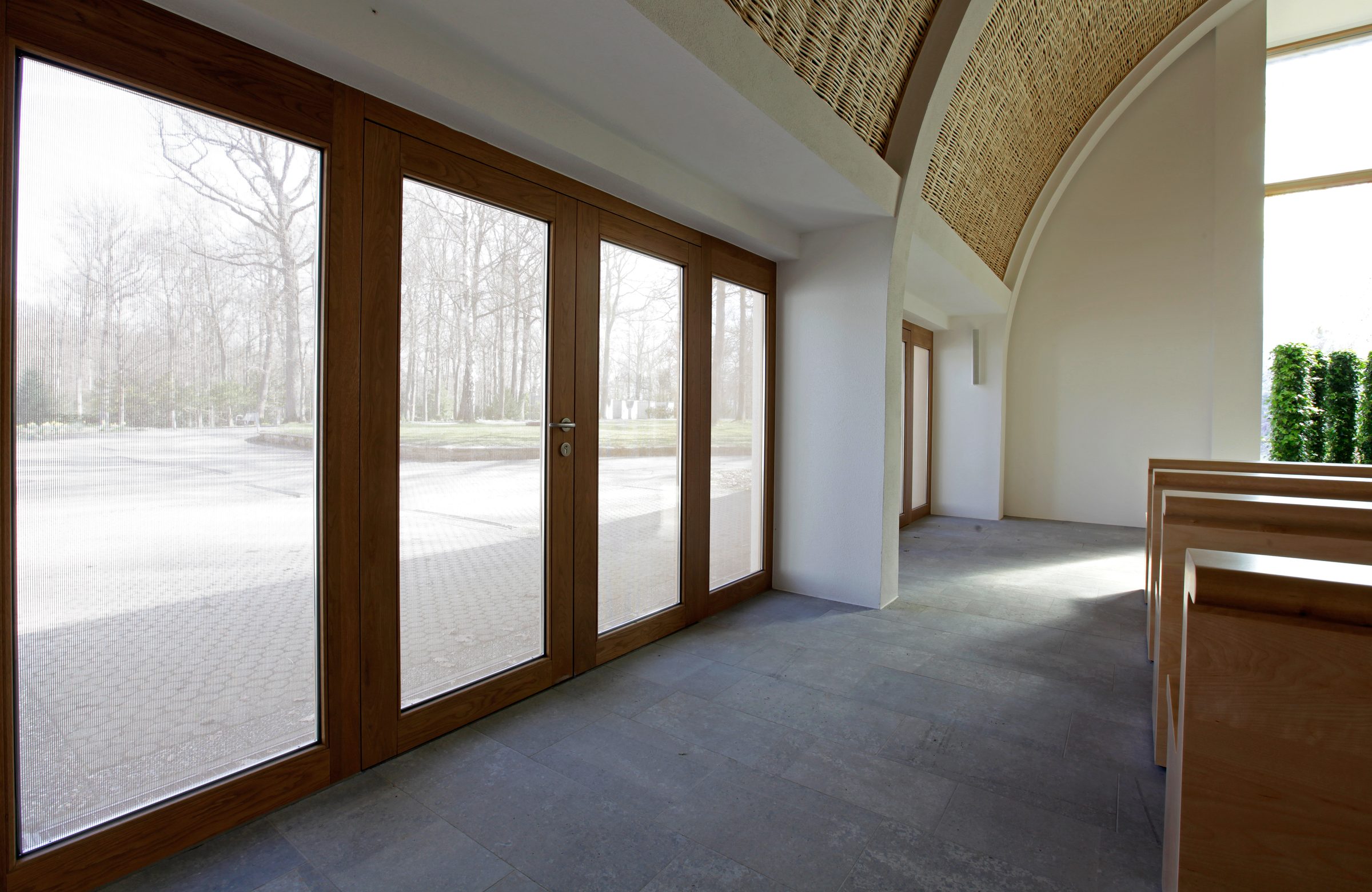 Aussegnungshalle Waldfriedhof Aalen, OKATECH Mandarin in entry door and side-aisle glazing, filtered daylight interior